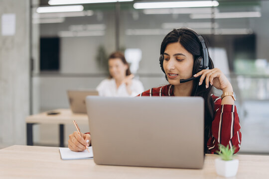 Customer support agent working in a call center, wearing a headset and talking with clients while making notes
