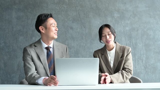 グレー背景で笑顔で会議をする日本人男女