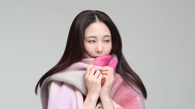 グレー背景の室内でマフラーに包まりながら笑顔を見せる30代の日本人女性