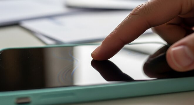 Close-up of a Finger Touching a Smartphone Screen with a Light Blue Case, Reflecting and Blurred