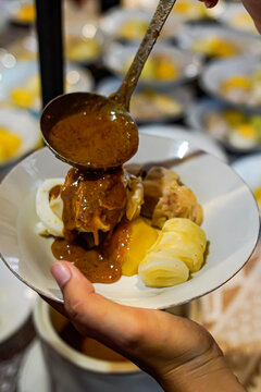 Close up of Indonesian siomay dumplings with egg and cabbage as peanut sauce is poured from ladle, authentic street food serving, Asian cuisine, warm lighting, food action moment