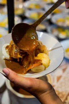 Close up of Indonesian siomay dumplings with egg and cabbage as peanut sauce is poured from ladle, authentic street food serving, Asian cuisine, warm lighting, food action moment