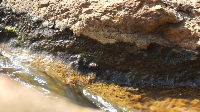 the view of a small natural stream or water puddle flowing through cracked and weathered brown stone boulders, showcasing detailed geological textures.