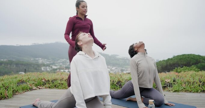 Diverse female yogis holding backbend on blue mats on deck, teacher approaching to guide form