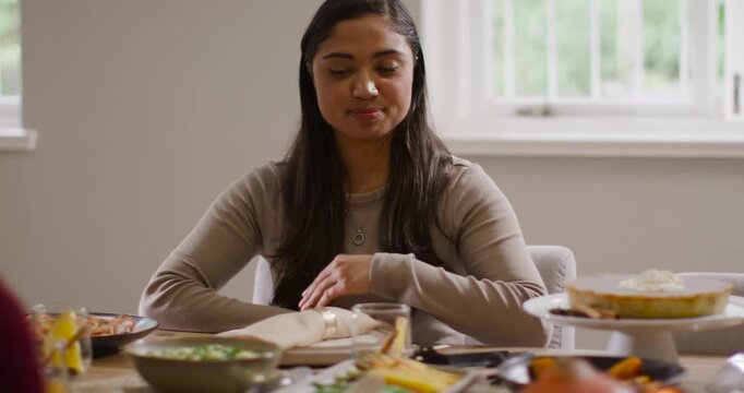 African American woman in beige top pointing at serving stand, maroon arm reaching, asking for dish