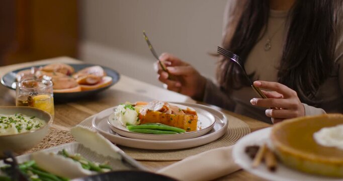African American woman reaching for fork and knife, cutting roasted squash and eating at table