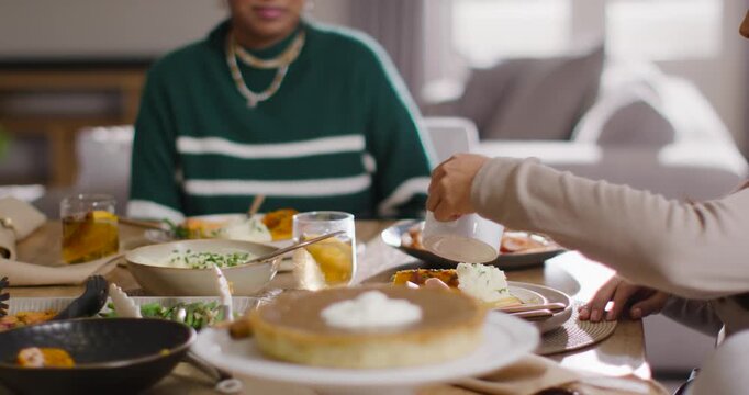 Diverse women at home green-sweater urging Indian pouring sauce from jug onto slice by cake-stand