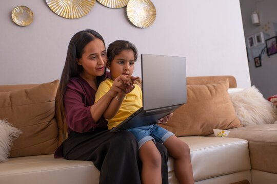 Mother and daughter playing video game on laptop on sofa in living room