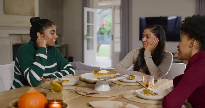 Diverse female friends sitting at dining table, left woman pointing and starting chat about pie