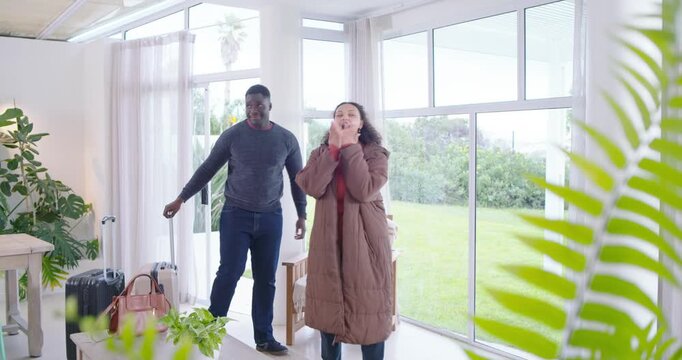 African American couple entering woman pulling suitcases and pink bag man following hugging in home