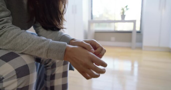 Adult female sitting near window in checkered pajamas holding round object, rotating, rubbing hands