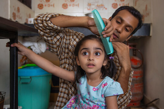 Father combing his daughter's hair in the kitchen