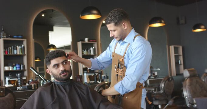 African American male barber placing hand, combing and cutting with scissors in shop to refine cut