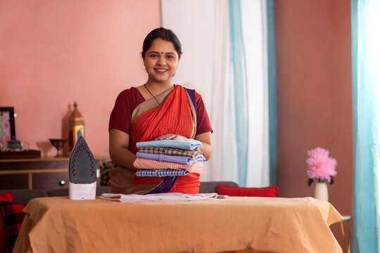 Portrait of a happy woman holding folded and ironed shirts