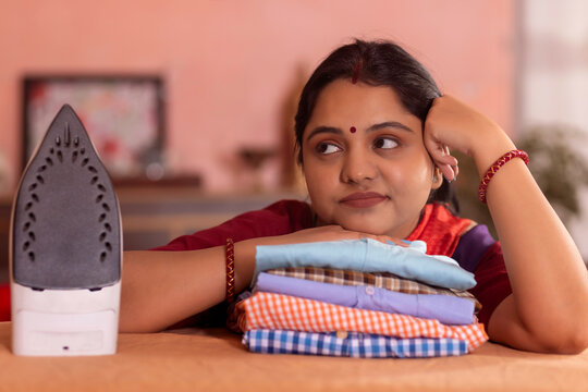 Close-up portrait of a sad woman looking away with resting her chin on ironed shirts