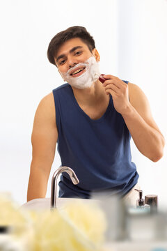 Young man applying shaving cream to his face in  bathroom at home