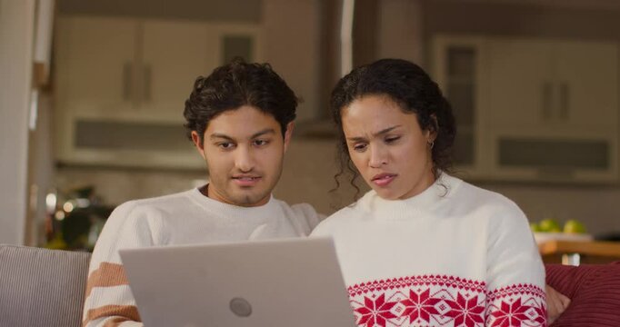 Couple sitting on couch viewing laptop, woman seeing unclear message, asking man then smiling