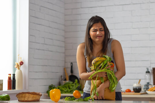 Woman standing in kitchen holding a heavy bag of vegetables