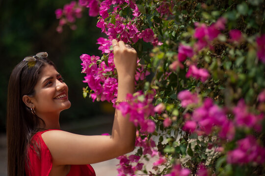 Portrait of young smiling woman standing near bougainvillea plant in the park