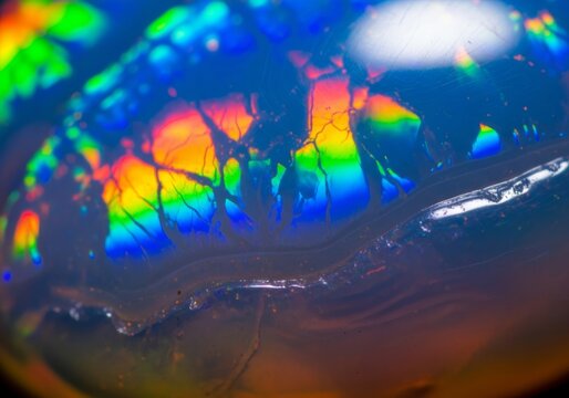 Extreme macro of opal gemstone displaying brilliant rainbow iridescence with blue green yellow and red flashes and dendritic cracks