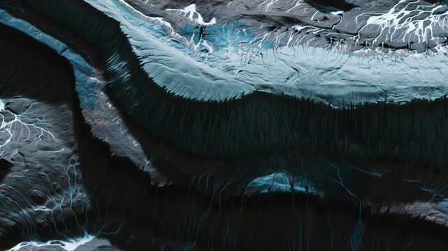 Aerial view shows layers of rock and soil patterns with water flowing through crevices. The scene captures various textures in a remote outdoor area.