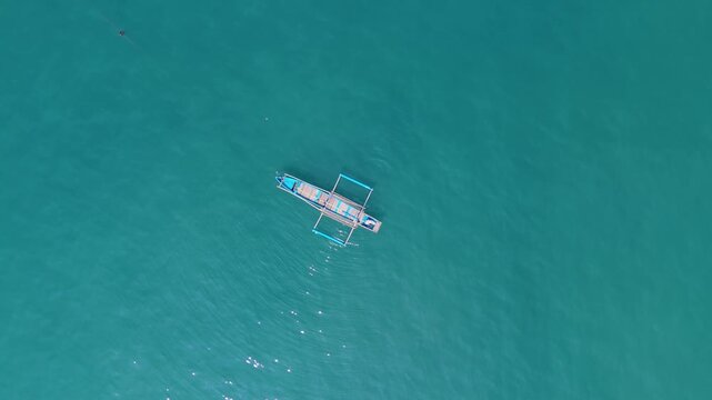 Aerial top view shows traditional fishing boat creating spiral wake across blue ocean