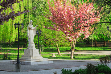 Obraz premium Serene religious sculpture stands amidst vibrant spring blossoms in a park