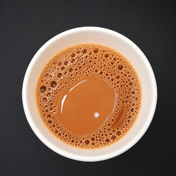 Top-down view of hot frothy milk tea (Chai) in a white cup on a dark background.