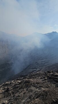 Camera panning over the spectacular steep rocky walls and texture of Bromo volcano caldera under a blue sky in Indonesia. Breathtaking geology video.