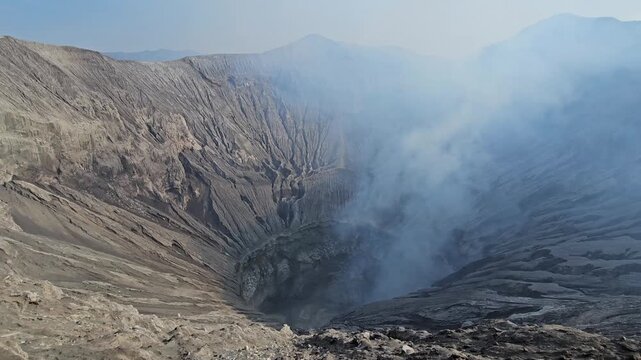 Camera panning over the spectacular steep rocky walls and texture of Bromo volcano caldera under a blue sky in Indonesia. Breathtaking geology video.