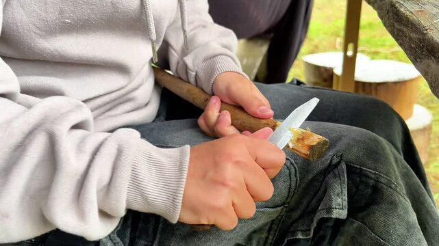 A person whittles the end of a wooden stick using a pocket knife. Suitable for outdoor survival brands, woodworking blogs, and scouting campaign promos.