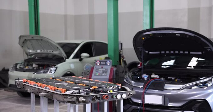 Professional EV technicians carefully removing the protective cover of a high-voltage battery pack before inspecting battery cells in a modern electric vehicle service workshop. T