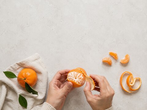 Manos pelando una mandarina en una mesa con una servilleta y gajos a su alrededor
