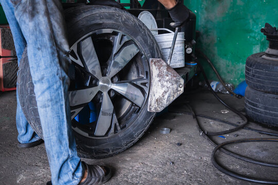 Mechanic using a pneumatic bead breaker shovel on a tire changing machine to separate rubber from the rim. Professional wheel demounting and tire service in an auto repair garage