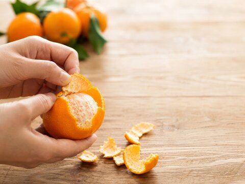 Mano pelando una mandarina en una mesa de madera con otras mandarinas al fondo