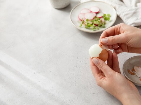 Pelar un huevo cocido en una mesa con ensalada de r&aacute;banos al fondo