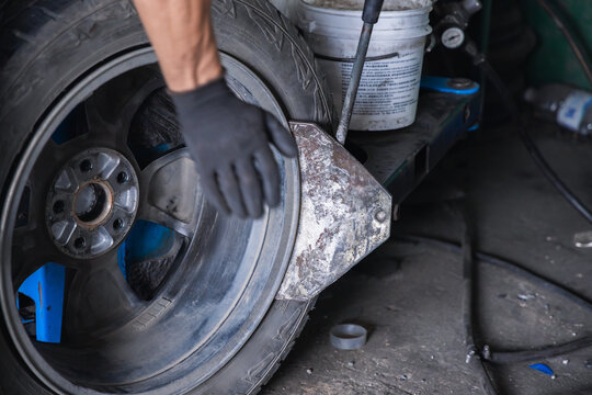 Mechanic using a pneumatic bead breaker shovel on a tire changing machine to separate rubber from the rim. Professional wheel demounting and tire service in an auto repair garage