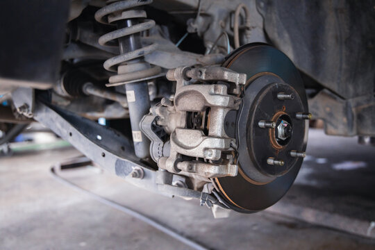 Exposed car suspension, brake disc, and shock absorber on an auto repair shop lift. Professional vehicle maintenance, undercarriage safety inspection, and fixing in a mechanic garage