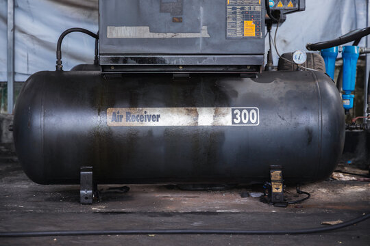 Large black industrial air receiver tank for a pneumatic compressor system in an auto repair garage. Heavy machinery and power source for mechanic workshop tools