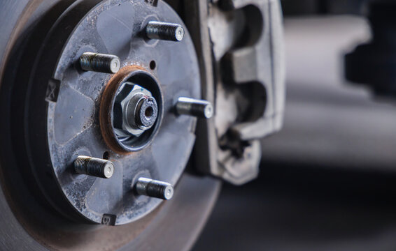 Close-up view of a car brake caliper, brake disc rotor, and wheel studs. Essential automotive parts exposed during a vehicle safety inspection and maintenance service in a mechanic shop