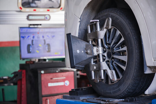 Wheel alignment target on a car tire with a diagnostic computer screen in the background. Modern auto repair technology for precise vehicle steering calibration