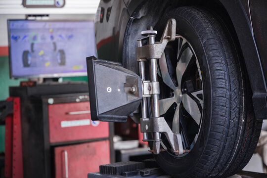 Wheel alignment target on a car tire with a diagnostic computer screen in the background. Modern auto repair technology for precise vehicle steering calibration