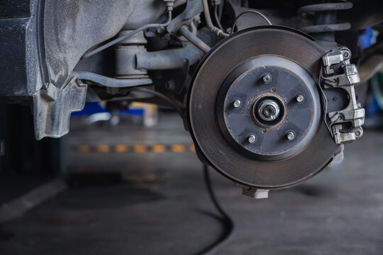 Exposed car suspension, brake disc, and shock absorber on an auto repair shop lift. Professional vehicle maintenance, undercarriage safety inspection, and fixing in a mechanic garage