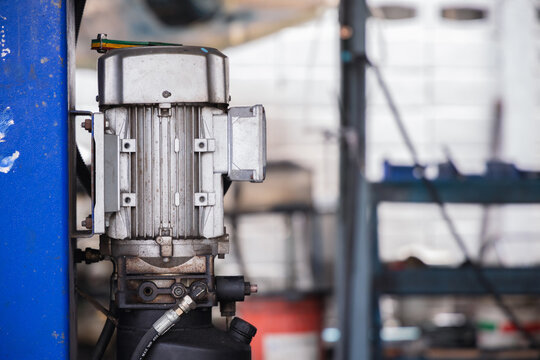 Electric motor and hydraulic pump system attached to a heavy-duty car lift post in an auto repair shop. Industrial machinery and garage equipment for professional vehicle maintenance