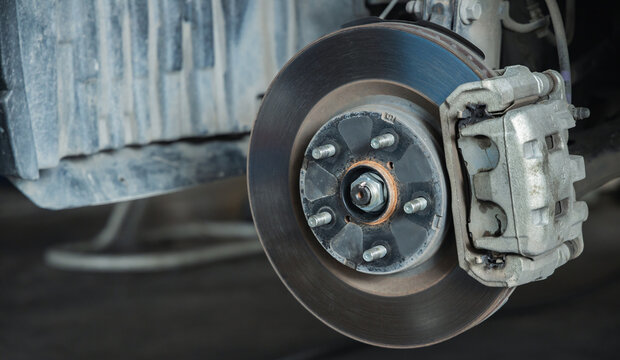 Close-up view of a car brake caliper, brake disc rotor, and wheel studs. Essential automotive parts exposed during a vehicle safety inspection and maintenance service in a mechanic shop