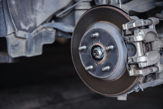Close-up view of a car brake caliper, brake disc rotor, and wheel studs. Essential automotive parts exposed during a vehicle safety inspection and maintenance service in a mechanic shop