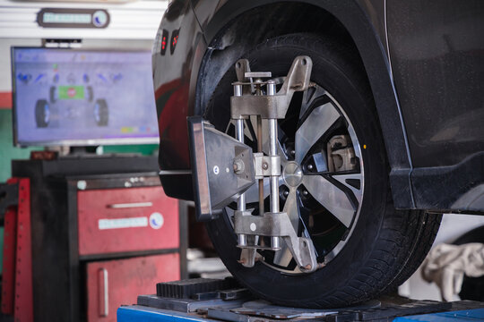 Wheel alignment target on a car tire with a diagnostic computer screen in the background. Modern auto repair technology for precise vehicle steering calibration