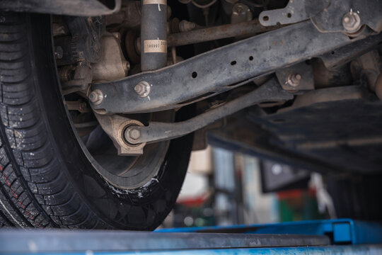 Car suspension system featuring a lower control arm and shock absorber. Vehicle undercarriage inspection and professional auto repair maintenance on a garage lift