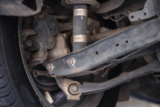 Car suspension system featuring a lower control arm and shock absorber. Vehicle undercarriage inspection and professional auto repair maintenance on a garage lift