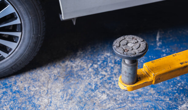 Heavy-duty rubber car lift pad and yellow support arm in an auto repair garage. Essential vehicle hoist safety equipment and machinery for professional automotive maintenance services